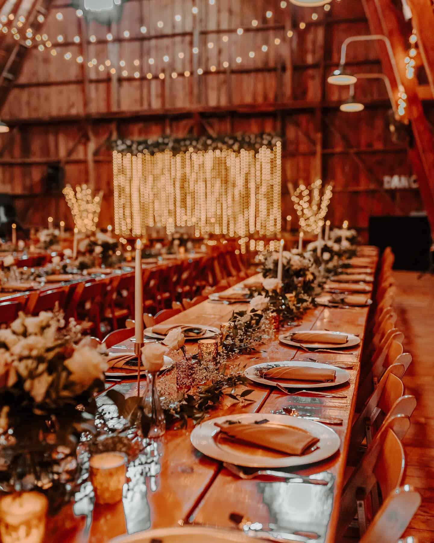 Elegant barn wedding reception decorated with string lights and floral centerpieces.