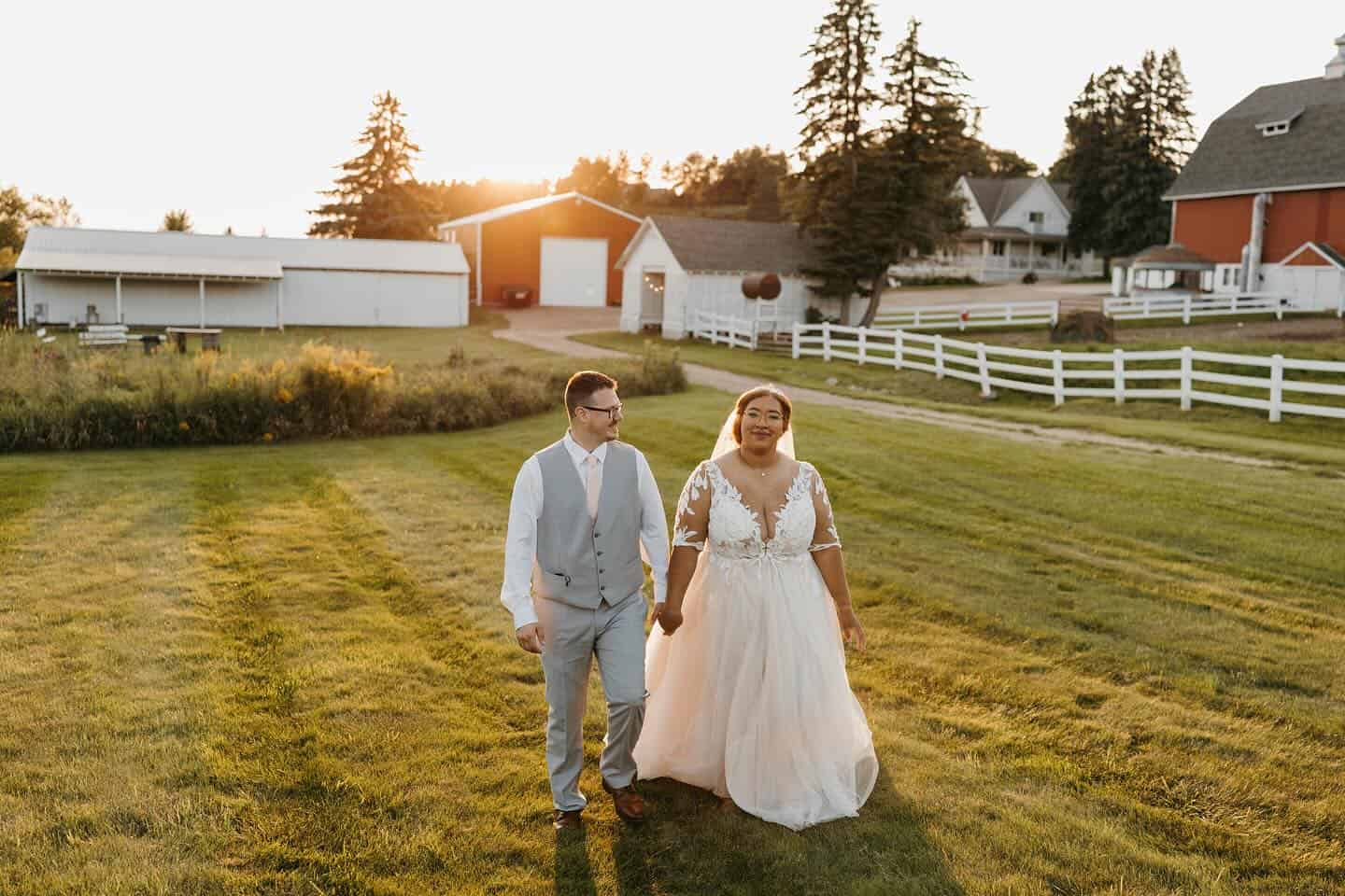 Happy bride and groom walking on the barn wedding venue at sunset.