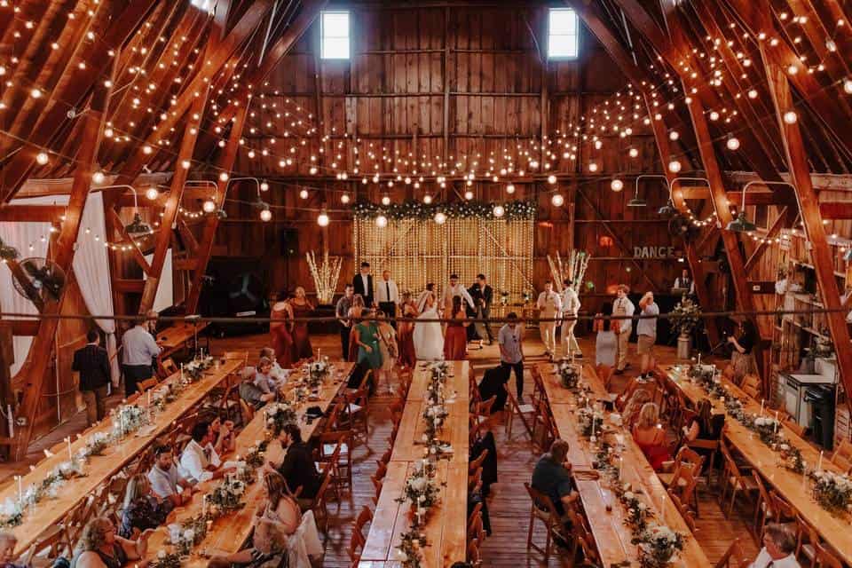 Rustic barn wedding reception with string lights and long tables for guests.