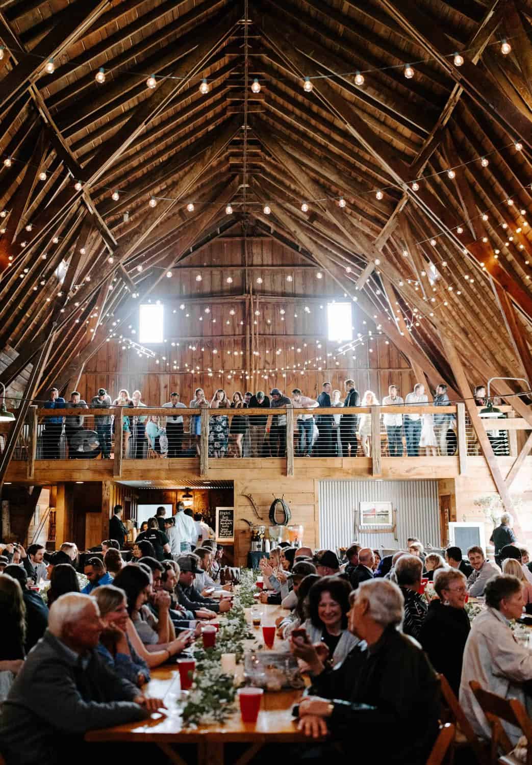 Elegant barn wedding reception with string lights and wooden beams.