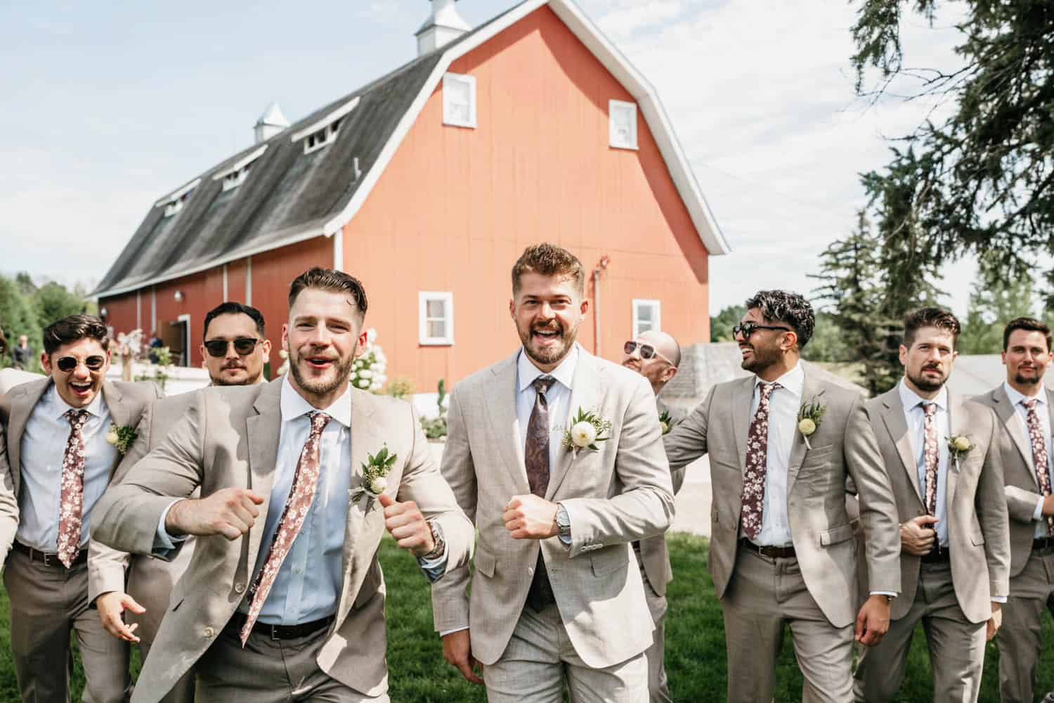Groomsmen in suits celebrating at Dellwood Barn wedding venue, outdoor wedding with lush greenery.