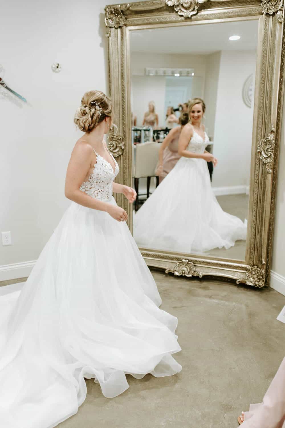 Bride in wedding gown looking at herself in a large ornate mirror.