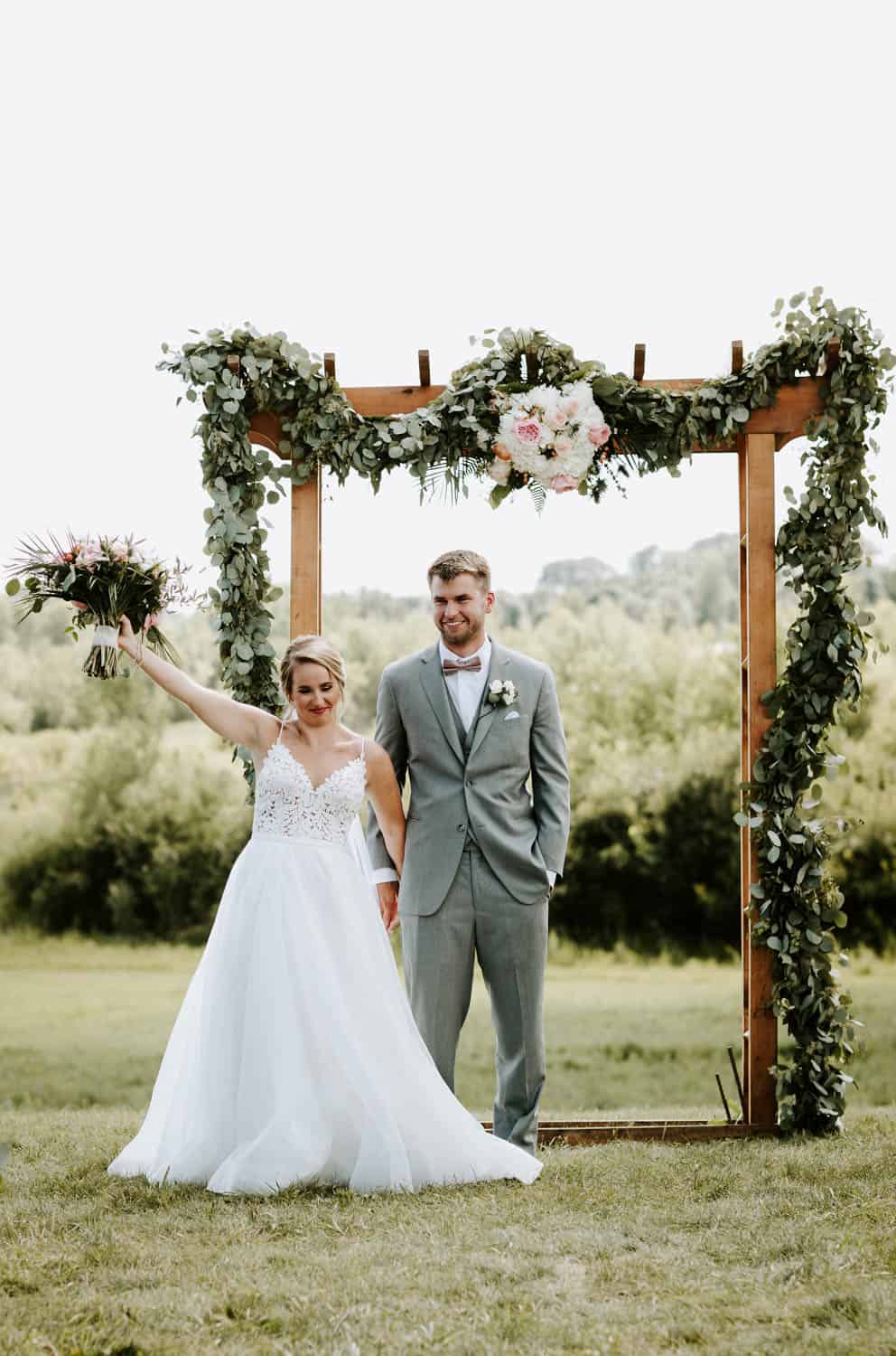 Outdoor wedding ceremony at Dellwood Barn with floral arch and happy couple.